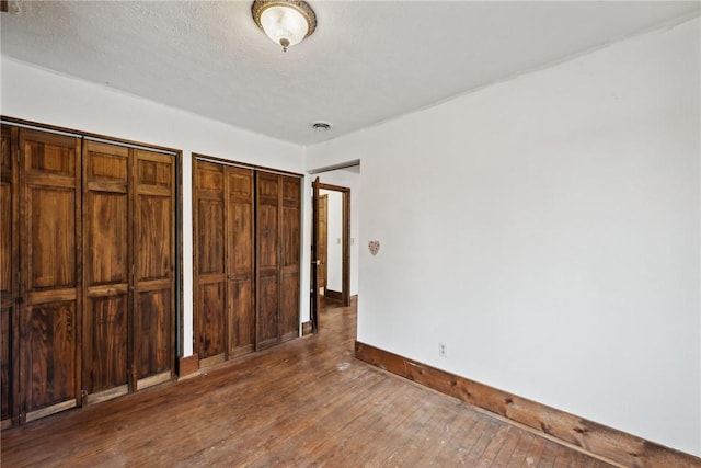 unfurnished bedroom featuring visible vents, baseboards, multiple closets, hardwood / wood-style flooring, and a textured ceiling