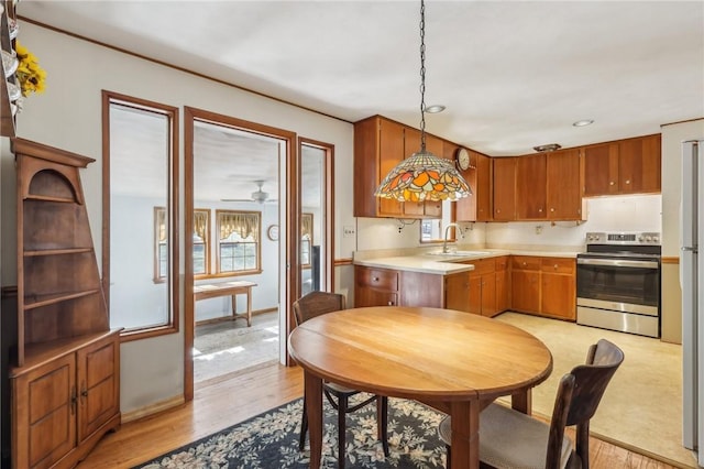 kitchen with a sink, decorative light fixtures, light wood finished floors, stainless steel electric range oven, and light countertops