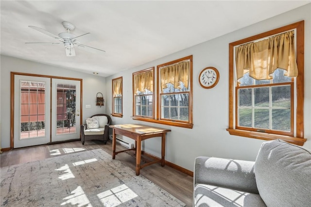 sitting room featuring a baseboard heating unit, wood finished floors, a ceiling fan, and baseboards