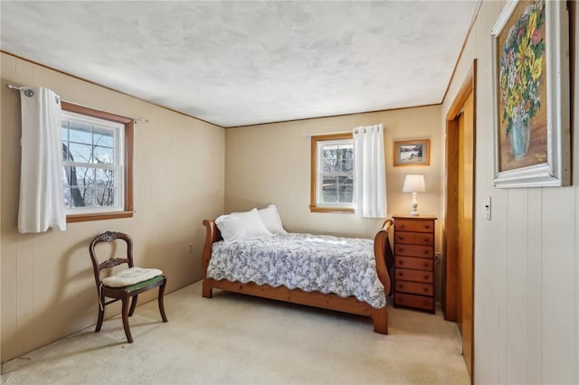 bedroom with light carpet, wooden walls, and multiple windows