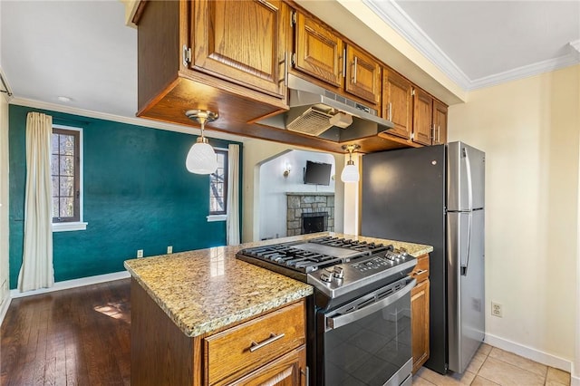 kitchen featuring stainless steel gas stove, brown cabinets, ornamental molding, under cabinet range hood, and light stone counters