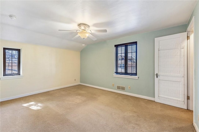 carpeted spare room featuring a wealth of natural light, visible vents, baseboards, and a ceiling fan