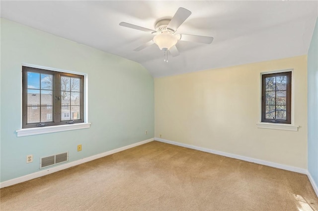 spare room featuring a ceiling fan, baseboards, visible vents, lofted ceiling, and light carpet