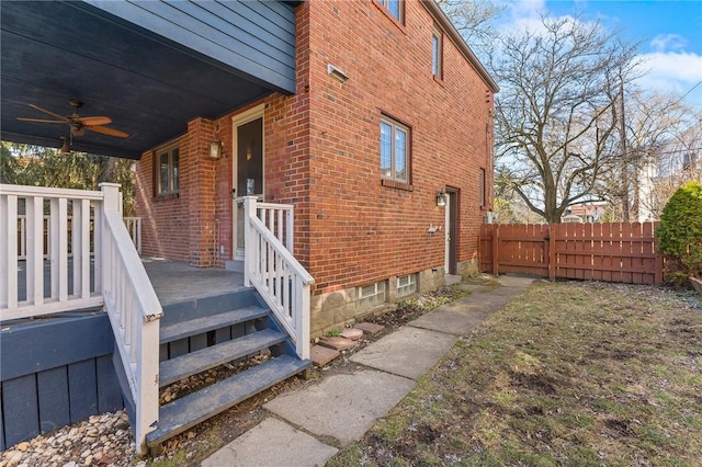 view of side of property with brick siding, ceiling fan, and fence