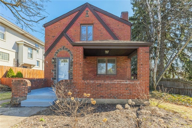 view of front of home with brick siding, a chimney, and fence