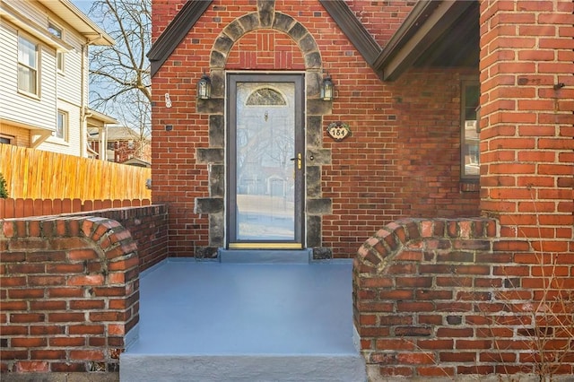 view of exterior entry featuring brick siding and fence