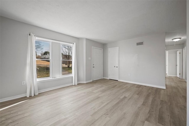 unfurnished living room with visible vents, a textured ceiling, baseboards, and wood finished floors