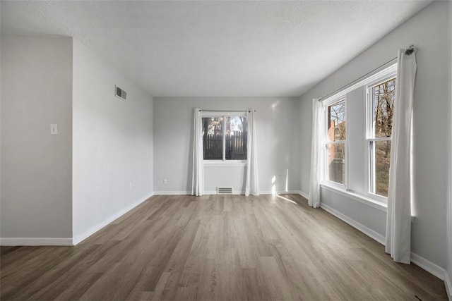 unfurnished room featuring visible vents, a textured ceiling, baseboards, and wood finished floors