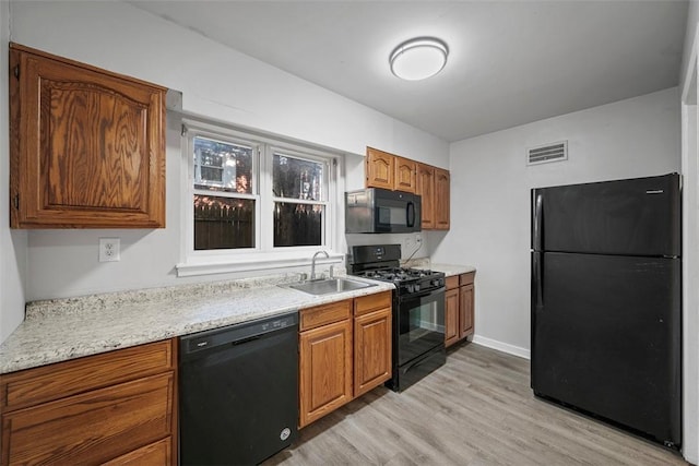 kitchen featuring visible vents, black appliances, a sink, light wood-style floors, and brown cabinetry