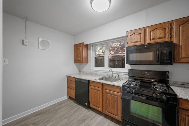 kitchen with light wood finished floors, light countertops, brown cabinetry, black appliances, and a sink