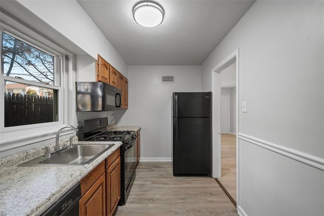 kitchen featuring brown cabinetry, visible vents, light wood-style flooring, a sink, and black appliances