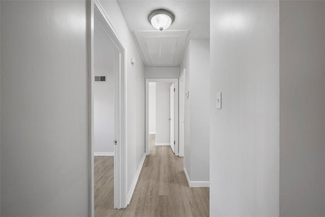 hall with visible vents, light wood-style flooring, attic access, and baseboards