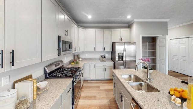 kitchen featuring light stone counters, light wood-style floors, appliances with stainless steel finishes, and a sink