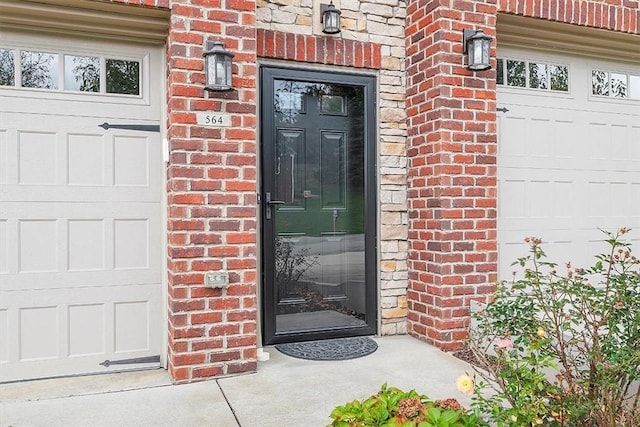 view of exterior entry featuring a garage and brick siding