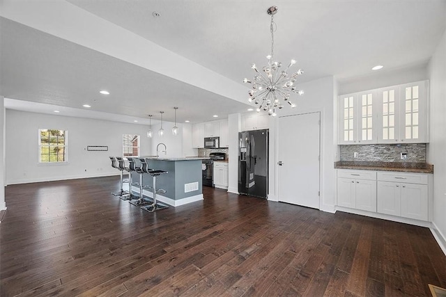 kitchen featuring dark wood finished floors, black appliances, an inviting chandelier, and a breakfast bar