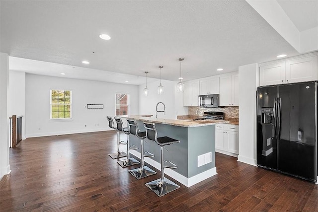 kitchen with black appliances, an island with sink, light stone counters, dark wood finished floors, and decorative backsplash