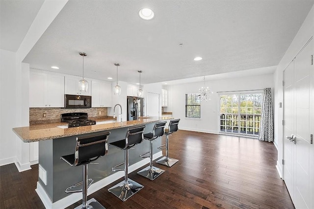 kitchen featuring dark wood-style floors, decorative backsplash, black appliances, white cabinetry, and a chandelier