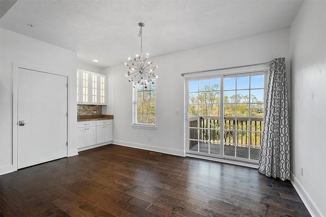 unfurnished dining area with a textured ceiling, recessed lighting, an inviting chandelier, baseboards, and dark wood-style flooring