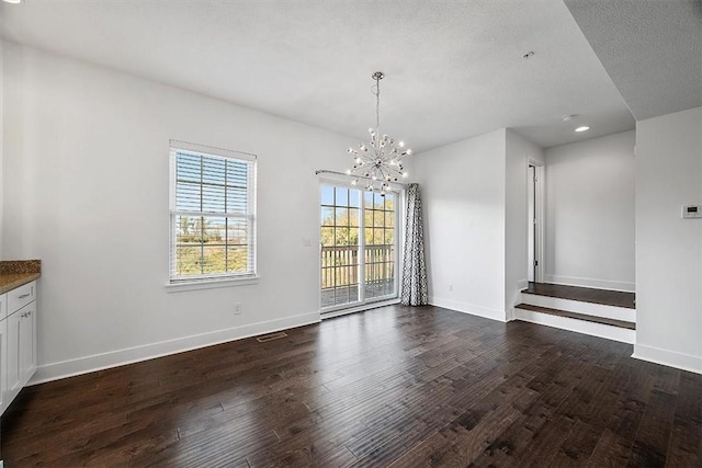 unfurnished dining area featuring an inviting chandelier, dark wood-type flooring, visible vents, and baseboards