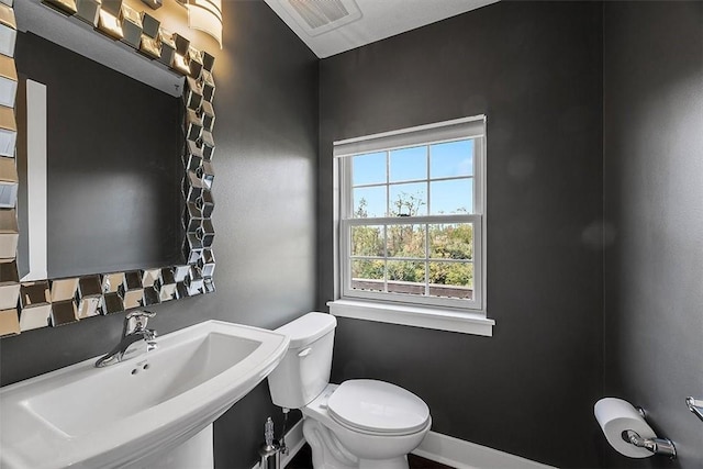 half bathroom featuring visible vents, toilet, baseboards, and a sink