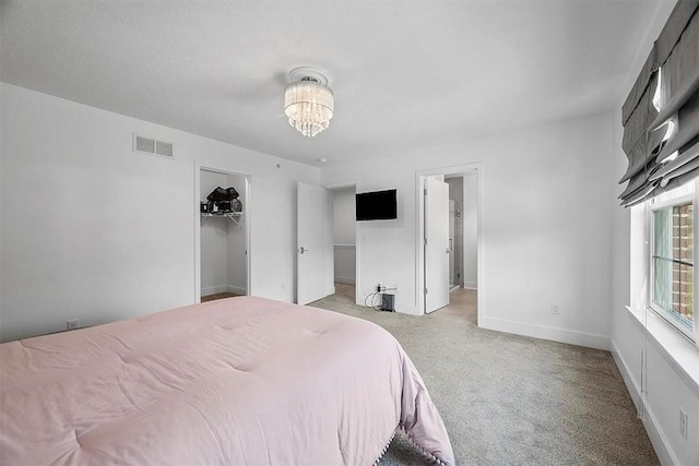 bedroom with a spacious closet, visible vents, baseboards, light colored carpet, and a notable chandelier