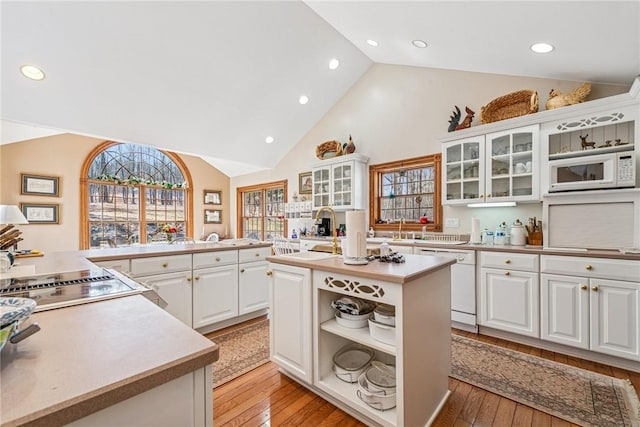 kitchen with white appliances, a center island with sink, open shelves, a sink, and light countertops