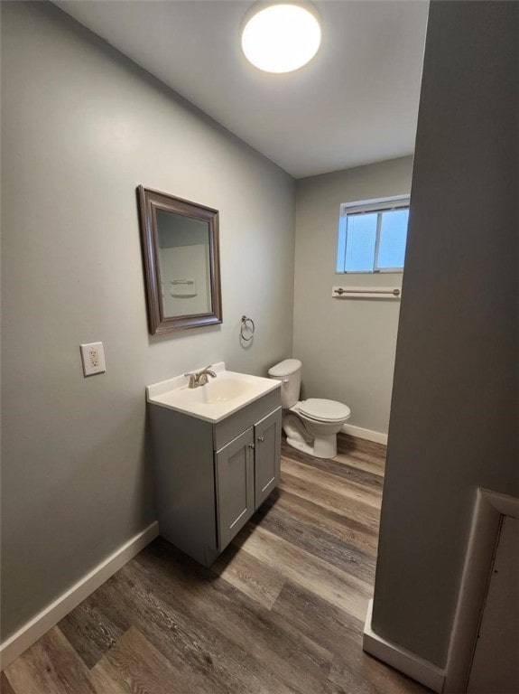 bathroom with toilet, vanity, baseboards, and wood finished floors