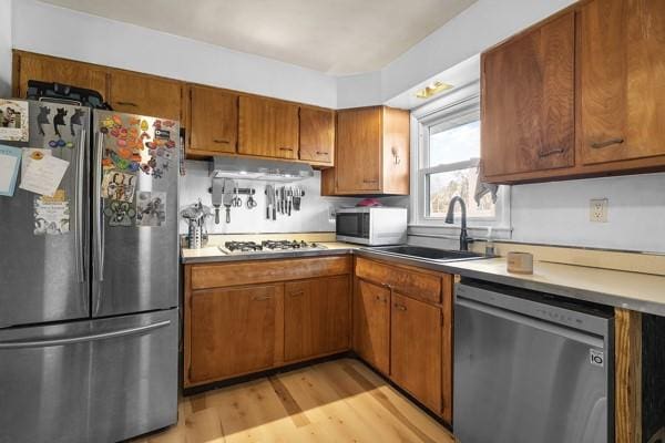 kitchen featuring light wood-type flooring, brown cabinets, a sink, range hood, and stainless steel appliances