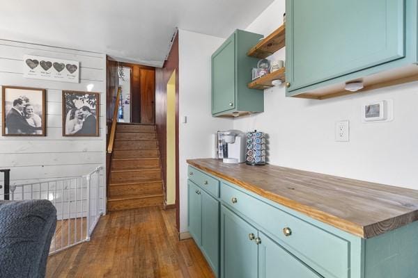 kitchen with green cabinetry, open shelves, dark wood-type flooring, wood walls, and wood counters