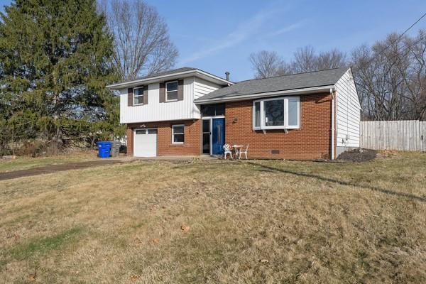 split level home with a front lawn, an attached garage, fence, and brick siding