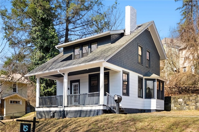 bungalow featuring a front yard, a porch, a chimney, and roof with shingles