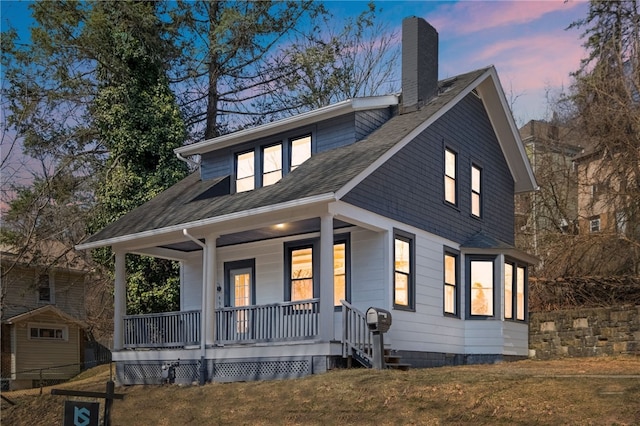 bungalow featuring a front yard, covered porch, roof with shingles, and a chimney