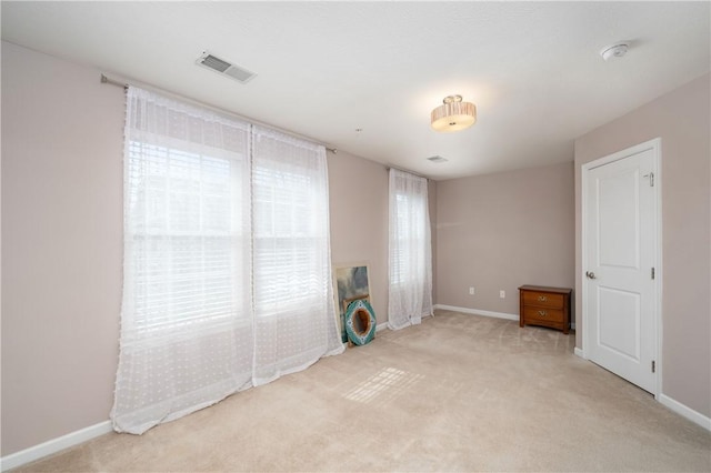 unfurnished room with visible vents, light colored carpet, and baseboards