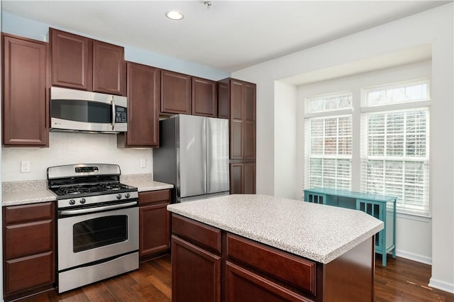 kitchen featuring a kitchen island, dark wood-type flooring, baseboards, light countertops, and stainless steel appliances