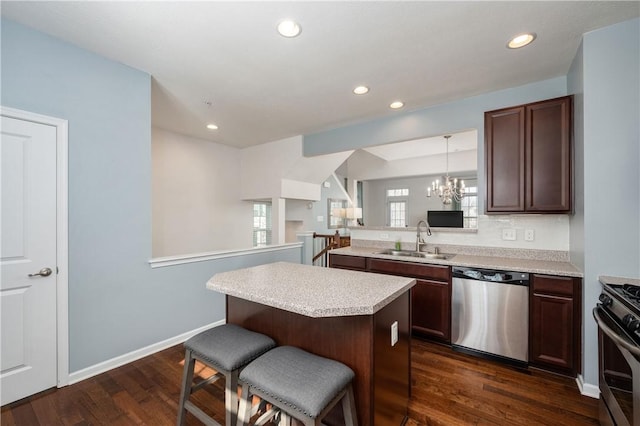 kitchen featuring a kitchen bar, a sink, dark wood finished floors, appliances with stainless steel finishes, and light countertops