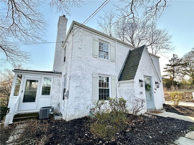exterior space featuring central AC unit, brick siding, and a chimney
