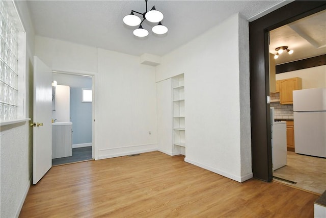 unfurnished room featuring baseboards, light wood-style floors, and a chandelier