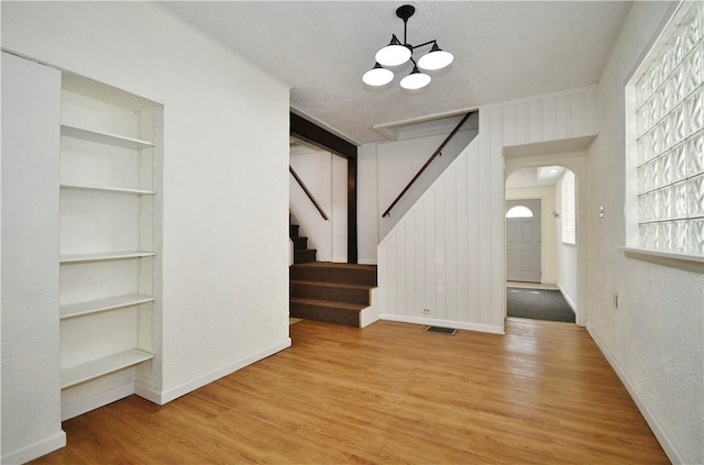 unfurnished living room with wood finished floors, visible vents, an inviting chandelier, arched walkways, and stairs