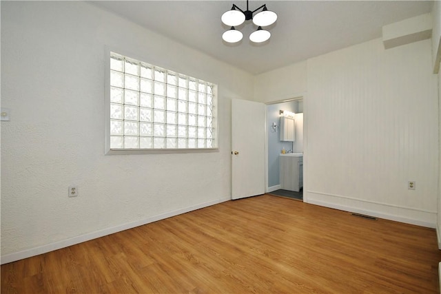 spare room with visible vents, wood finished floors, baseboards, and a chandelier