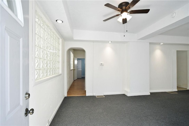 unfurnished room featuring baseboards, arched walkways, a raised ceiling, a ceiling fan, and dark colored carpet