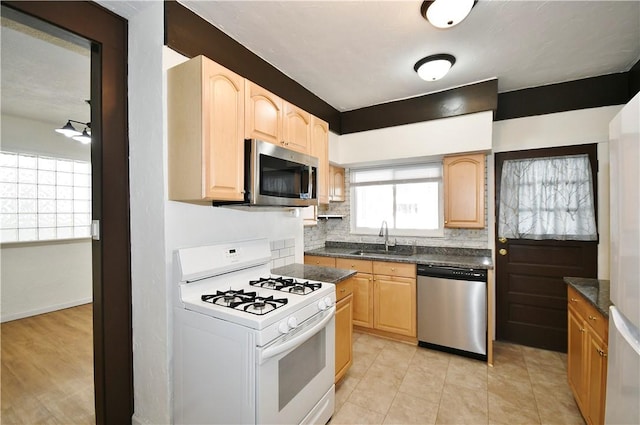 kitchen with tasteful backsplash, dark countertops, light brown cabinets, appliances with stainless steel finishes, and a sink