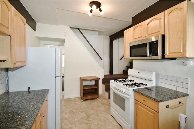 kitchen with light tile patterned floors, dark stone counters, white appliances, and light brown cabinets