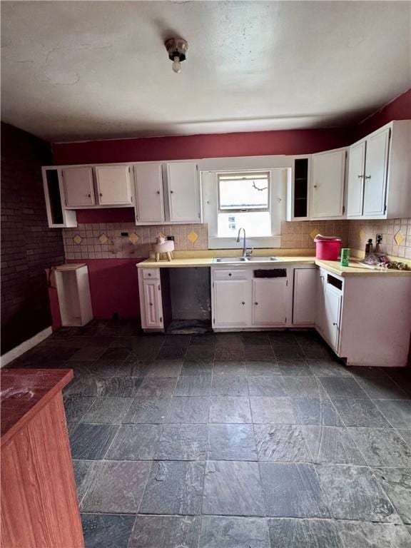 kitchen featuring tasteful backsplash, white cabinets, stone finish floor, and a sink