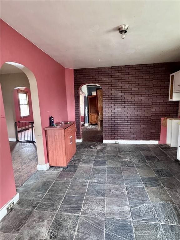 interior space with baseboards, arched walkways, and brick wall