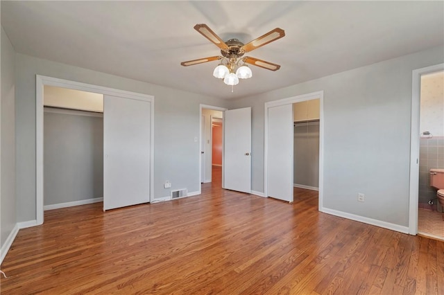 unfurnished bedroom with visible vents, a ceiling fan, wood finished floors, connected bathroom, and baseboards