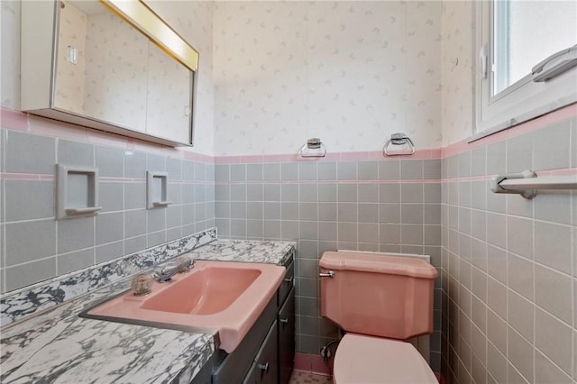 half bathroom featuring wallpapered walls, toilet, a wainscoted wall, and a sink