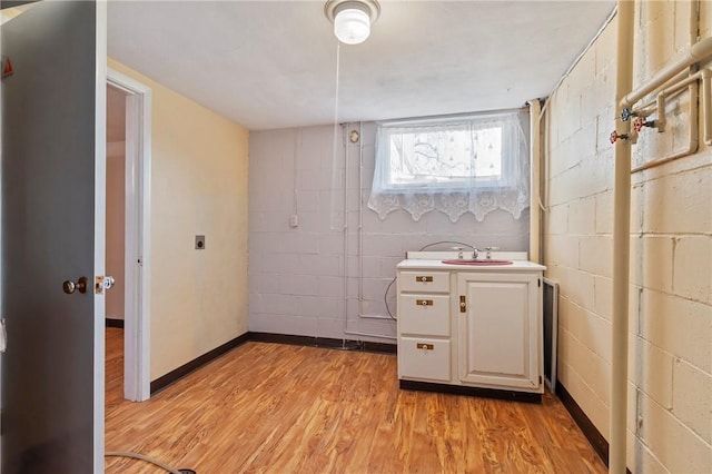 interior space featuring light wood-style flooring, concrete block wall, baseboards, and a sink