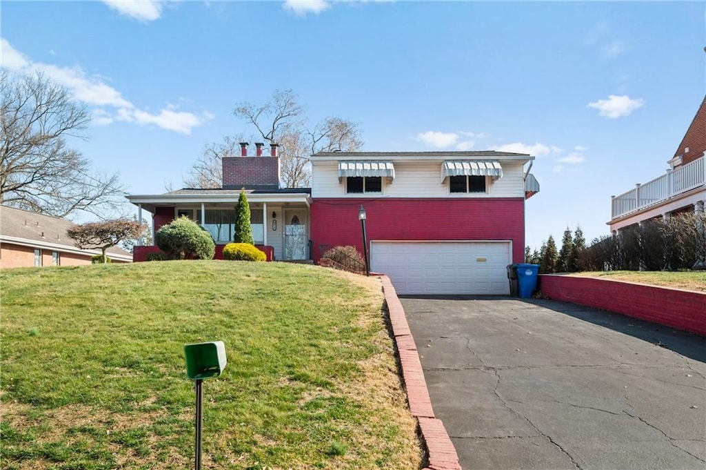 tri-level home with aphalt driveway, an attached garage, a chimney, and a front lawn