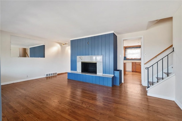 unfurnished living room with stairs, wood finished floors, visible vents, and baseboards