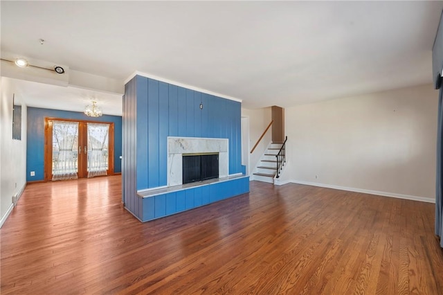 unfurnished living room with wood finished floors, stairway, an inviting chandelier, a fireplace, and baseboards